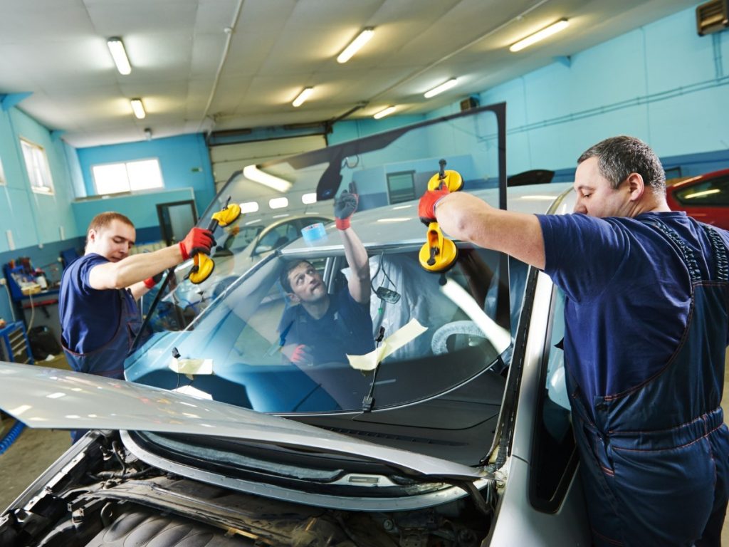 Two technicians at a windshield replacement shop in Evergreen Lawn, installing a new front windshield
