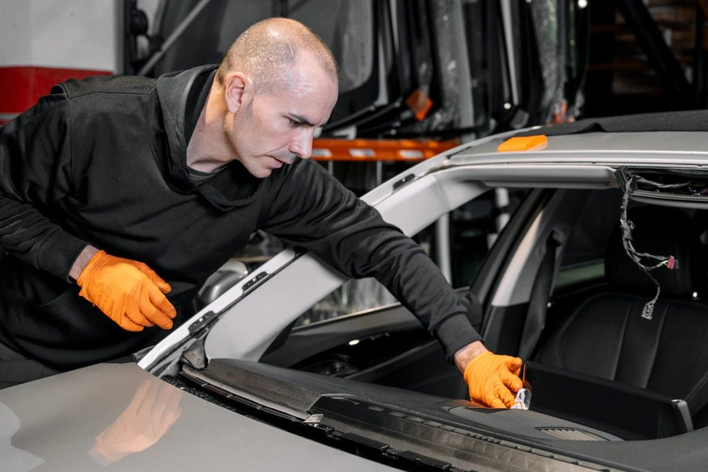 Expert technician in orange gloves removing damaged windshield during auto glass replacement in Baltimore workshop, ensuring precise and safe installation.
