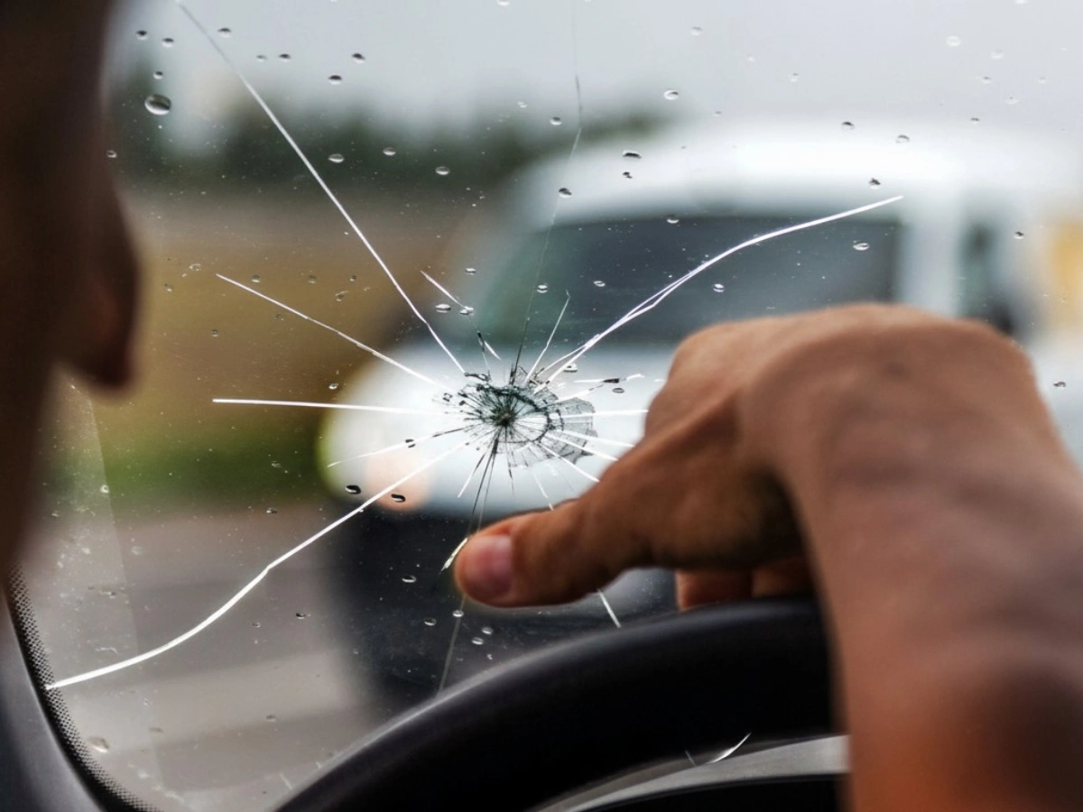 Close-up of a cracked car windshield with a hand pointing, highlighting urgent Mobile Auto Glass Repair Baltimore services.