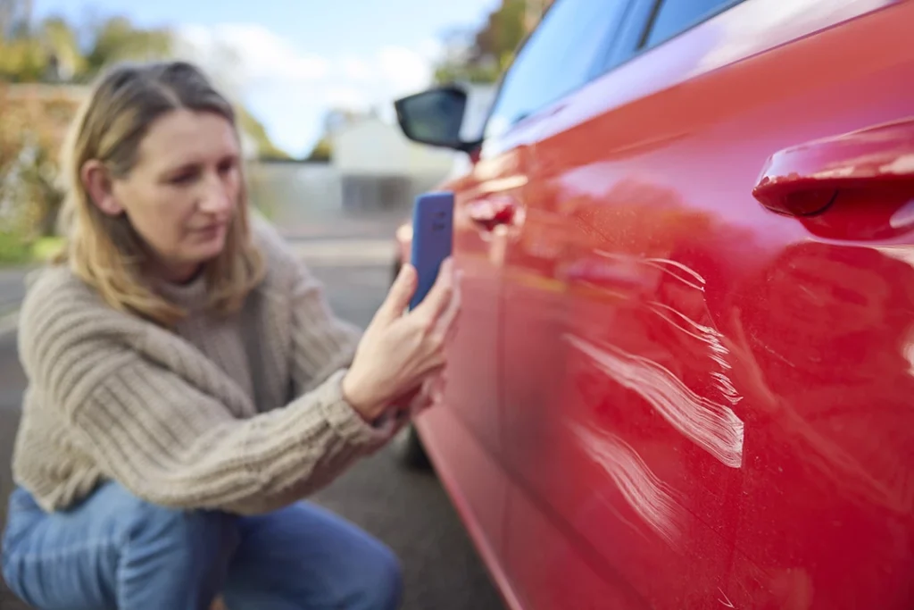 car owner inspecting scratches on red car - auto glass repair West Glen