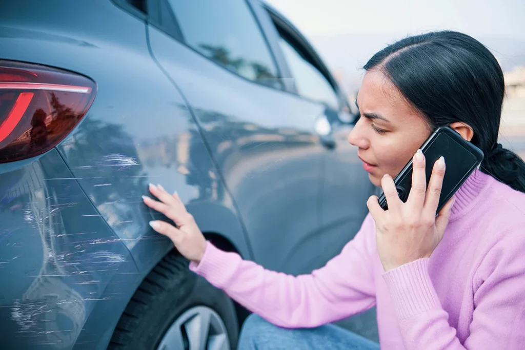 woman on phone examining scratches on her car - auto glass repair West Glen