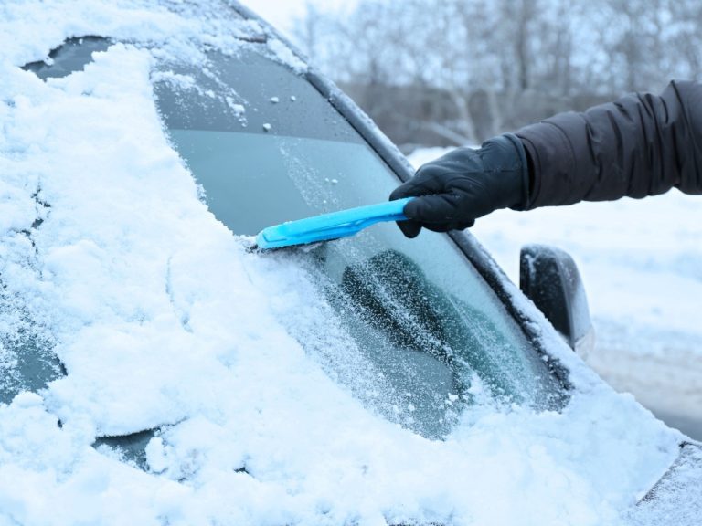 Icy windshield being scraped clear with a blue tool, a common issue that may require a windshield fix in Baltimore.