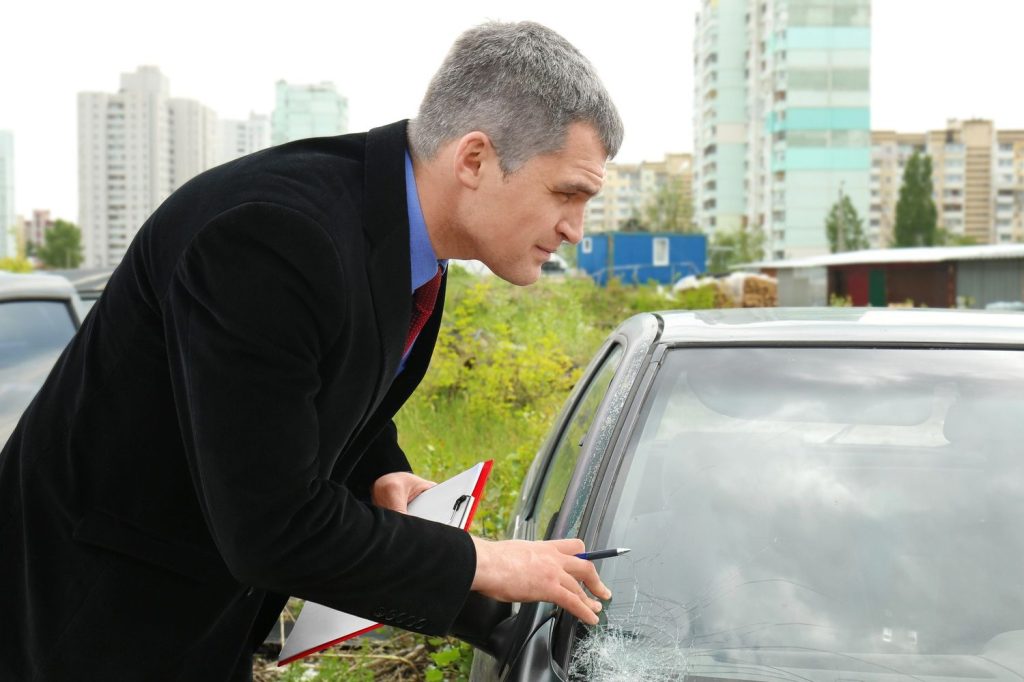 Auto glass fix in Baltimore: Inspector in suit meticulously examines a cracked car window with a clipboard in hand.