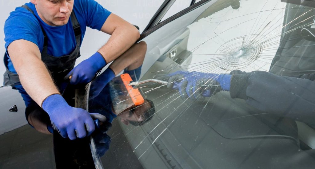 Auto glass fix in Baltimore: Skilled worker in blue uniform carefully repairs a cracked car windshield using specialized tools.