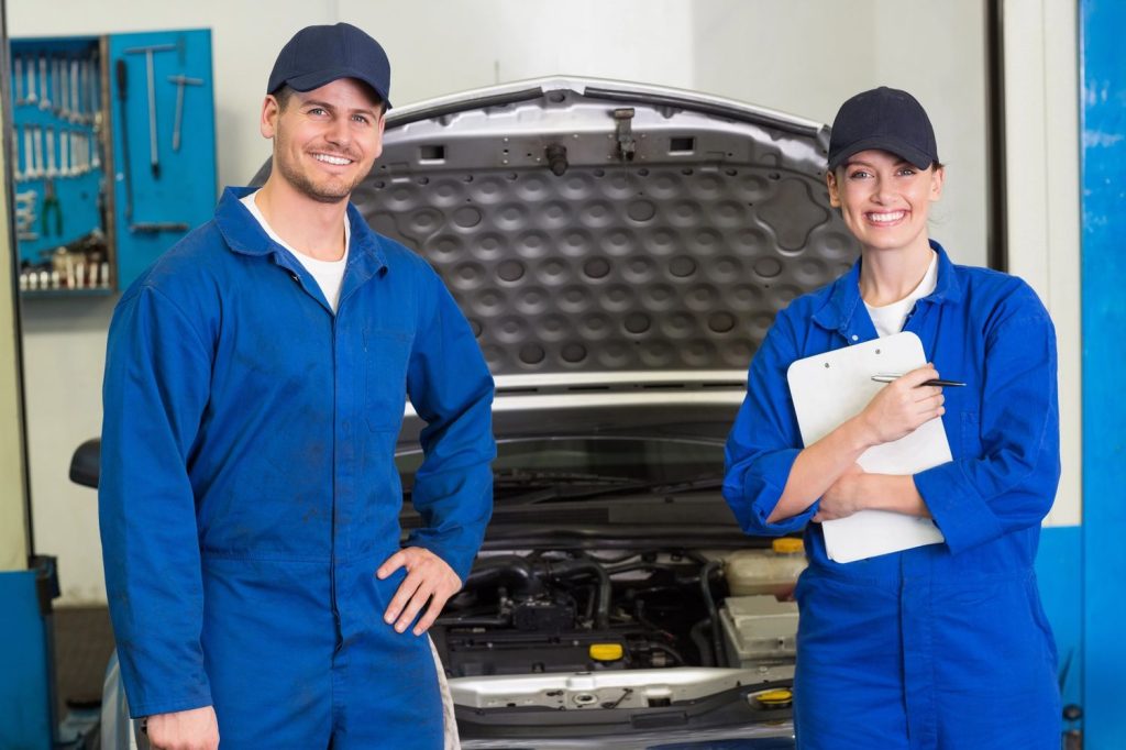Satisfied customer shaking hands with expert mechanic after windshield repair service in Baltimore, standing beside red car outdoors.