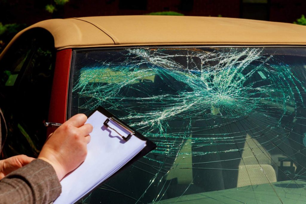 Auto glass repair shop Baltimore: Inspector examines a shattered car windshield with a clipboard.