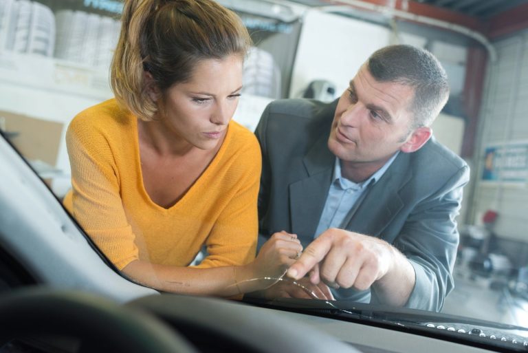 Auto glass repair shop Baltimore: Man and woman inspect a car windshield together in a repair shop setting.