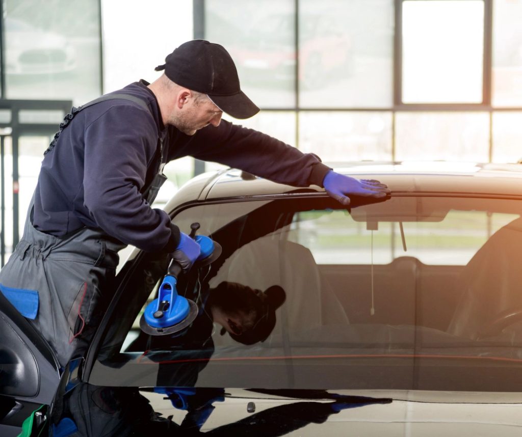Professional technician at auto glass shop Baltimore carefully applying suction cup tool to replace cracked car windshield in modern garage setting.