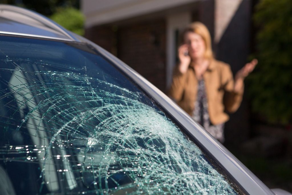 Auto glass repair shop Baltimore: Woman on phone near a car with a cracked windshield.