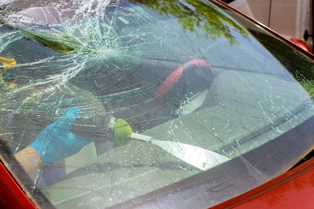 Auto glass repair shop Baltimore: Worker in gloves removes a shattered car windshield with tools outside.