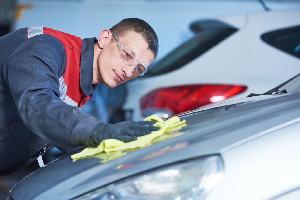Auto glass repair shop Baltimore: Worker in uniform cleans a car with a yellow cloth in a professional garage.