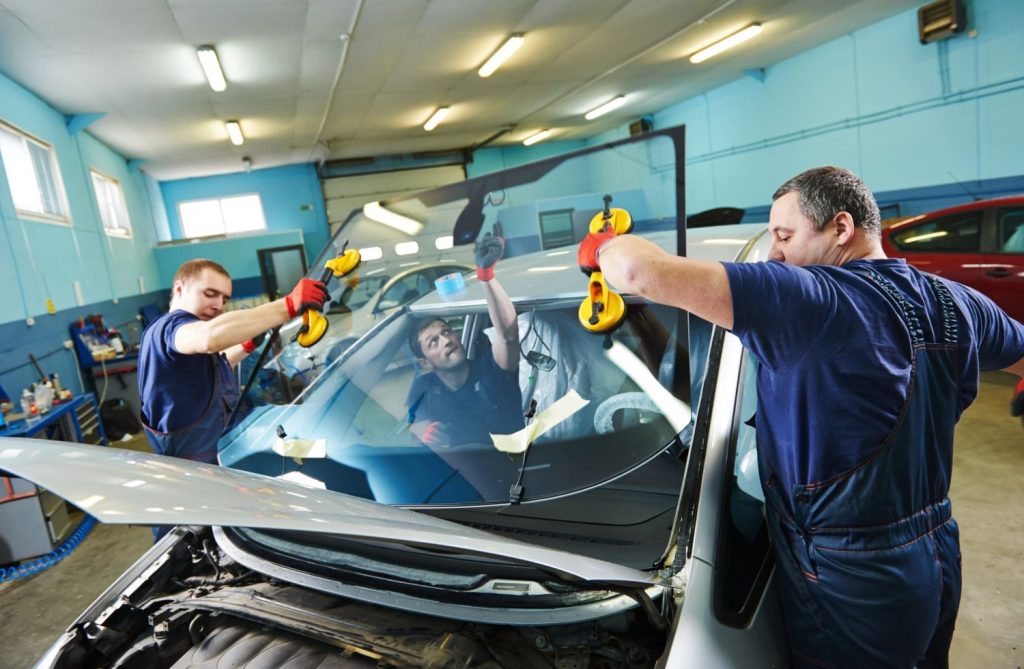 Professional technicians from mobile windshield repair Baltimore service lifting a car windshield with suction cups in a garage, ensuring precise installation for vehicle safety and clarity on the road.
