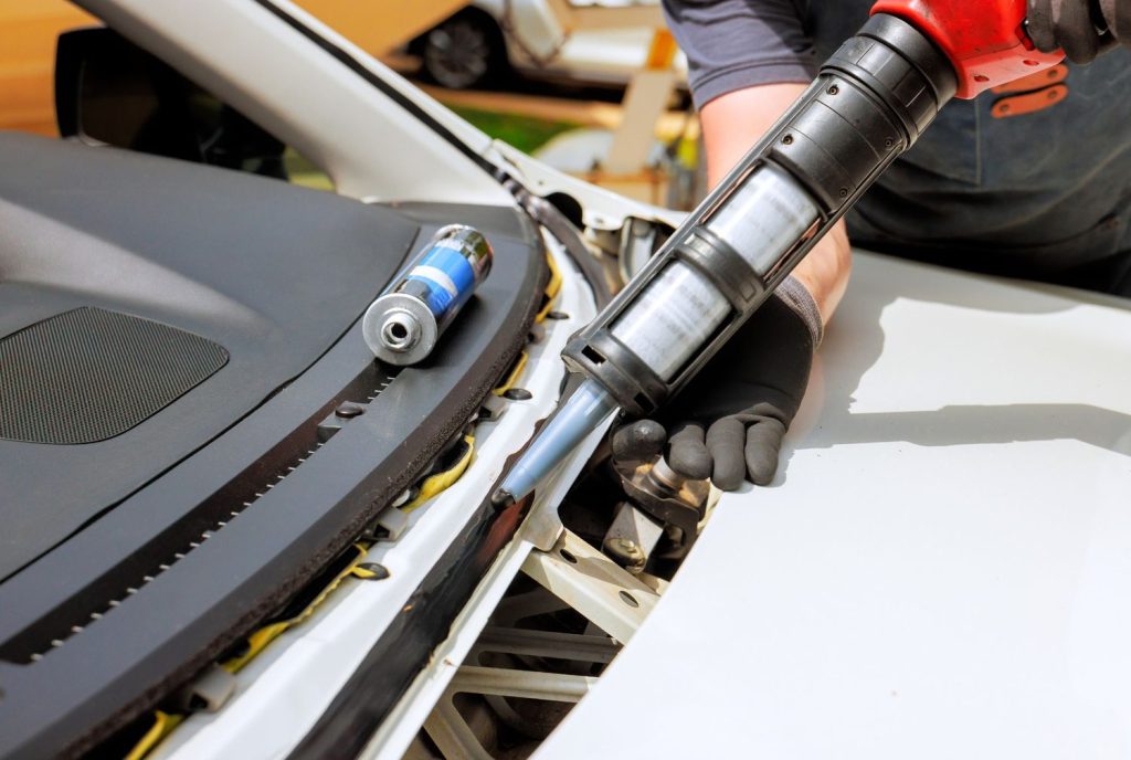 Close-up of a worker applying adhesive sealant for a quick car windshield fix Baltimore replacement.