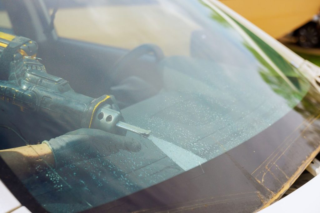 Specialist cutting the old seal with a saw tool for a quality car windshield fix Baltimore replacement.