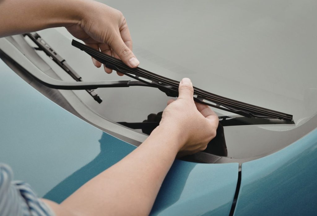 Close-up of hands replacing a wiper blade for a car windshield fix Baltimore service on a blue car.