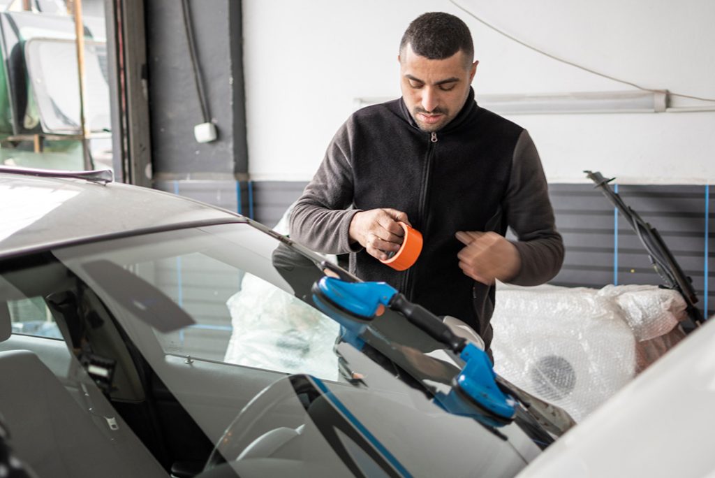 Auto glass company Baltimore technician using orange tape to secure a newly installed car windshield in a shop.