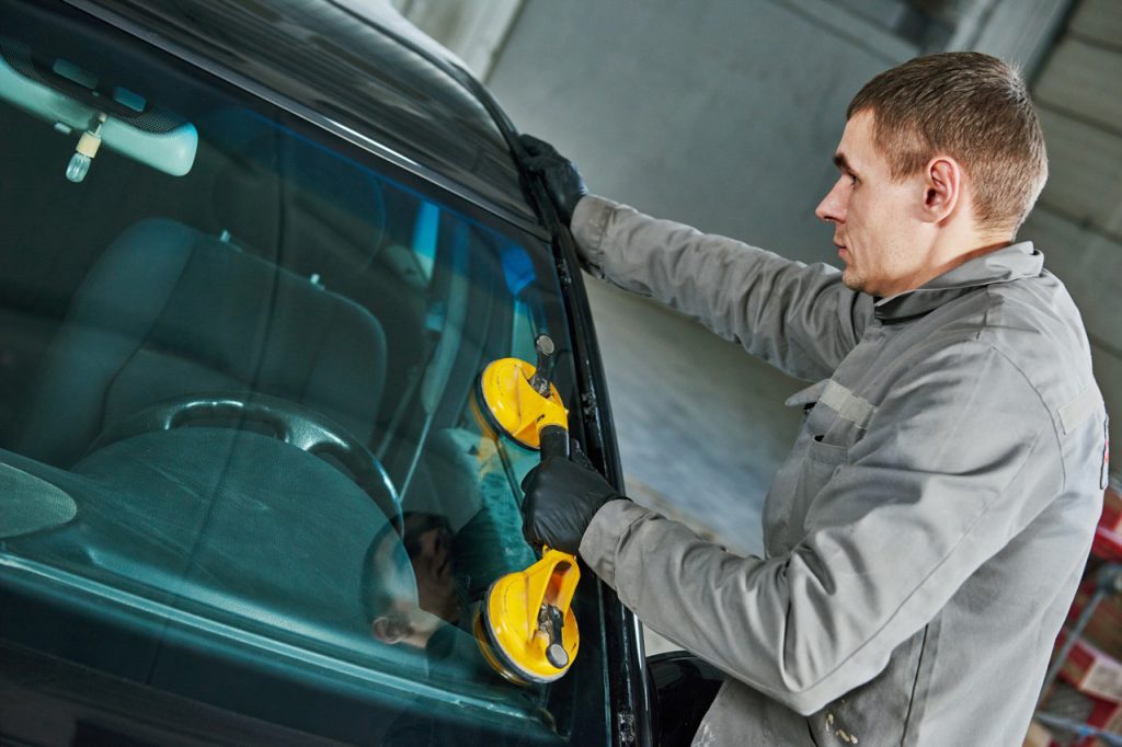 Expert auto glass fix Baltimore technician wearing gloves while carefully aligning a front car window replacement.