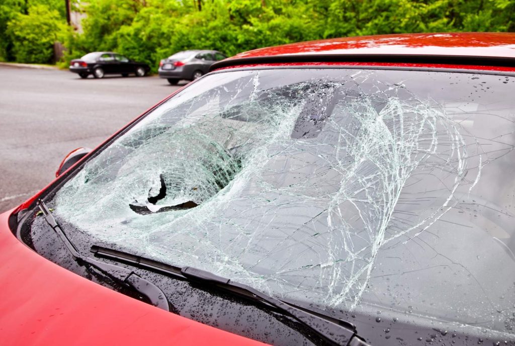Shattered windshield on a red car parked outdoors. Call the certified auto glass specialists in Baltimore for help now.
