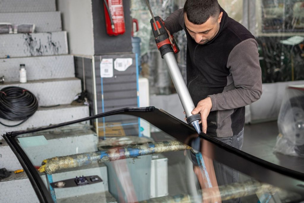 Applying adhesive sealant to a new windshield, a key step in quality glass car repair Baltimore service.