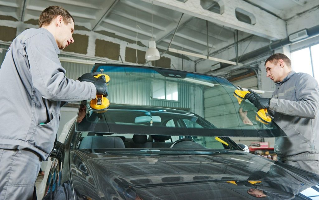 Two technicians install a new car windshield, providing expert glass car repair Baltimore for sedan models.
