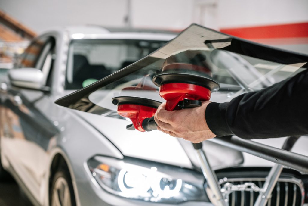 Close up of a technician performing an auto glass fix Baltimore service by lifting a new glass panel onto a car.