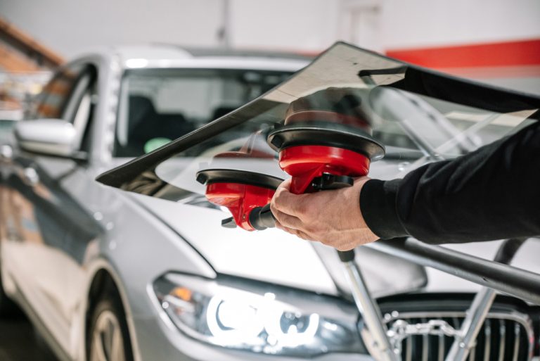 Close up of a technician performing an auto glass fix Baltimore service by lifting a new glass panel onto a car.