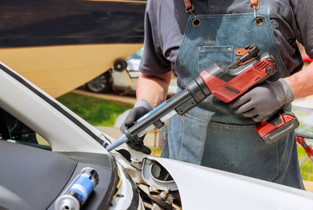 A technician uses an adhesive gun to apply sealant to a car frame during professional mobile windshield repair Baltimore.