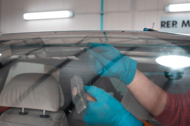 Auto glass technician wearing blue gloves applying resin to fix a chip from inside the vehicle for expert windshield repair service Baltimore.