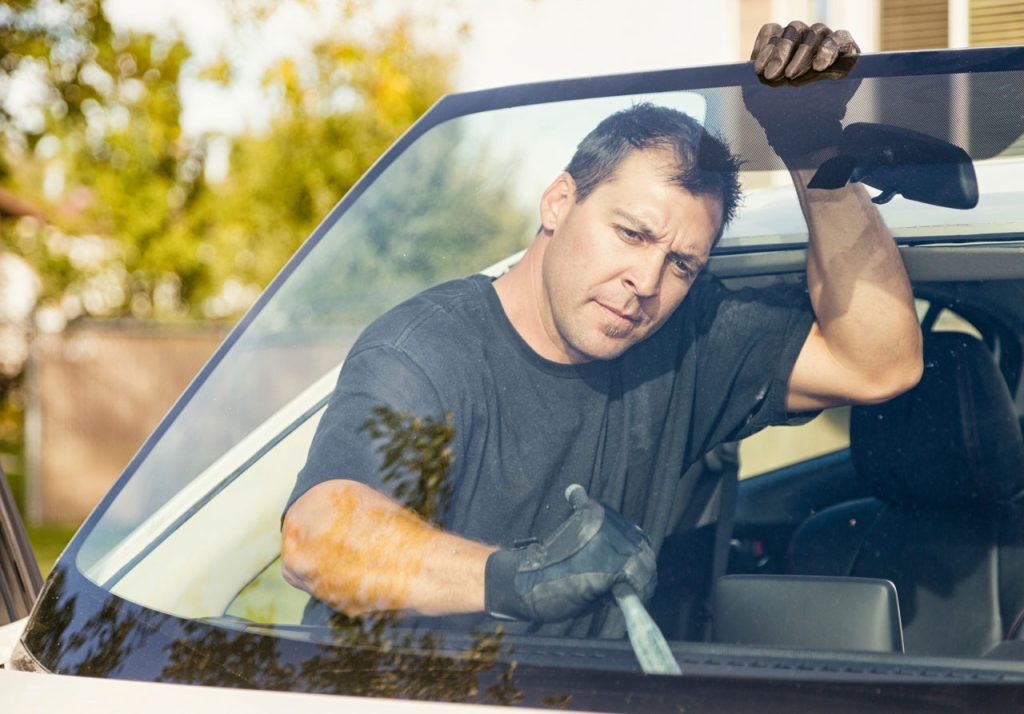 Skilled technician from an auto glass company Baltimore removing a damaged windshield using professional tools.
