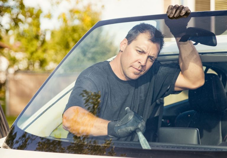 Skilled technician from an auto glass company Baltimore removing a damaged windshield using professional tools.