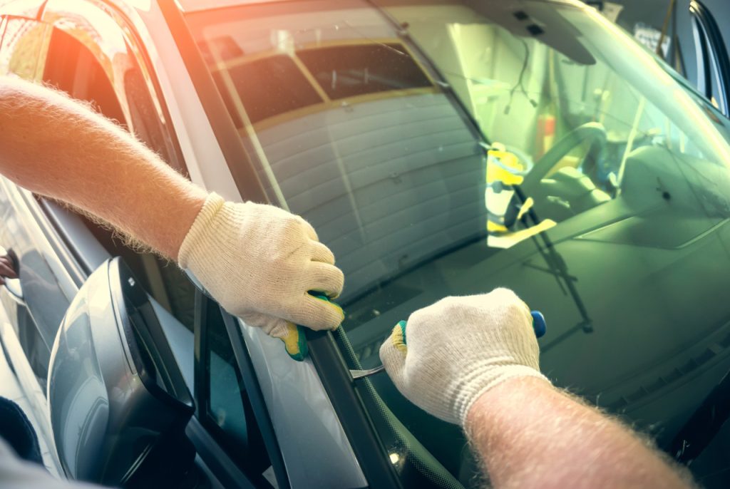 Professional technician at an auto glass company Baltimore removing a damaged windshield with specialized hand tools.