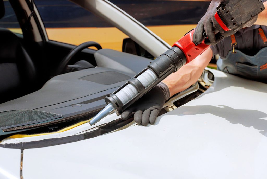 Expert auto glass fix Baltimore technician uses a professional tool to apply high-quality sealant to a car frame.