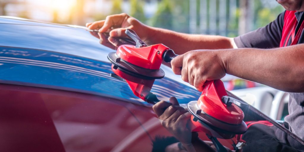 Expert auto glass replacement Baltimore services shown as a technician installs a new windshield on a red car outdoors.