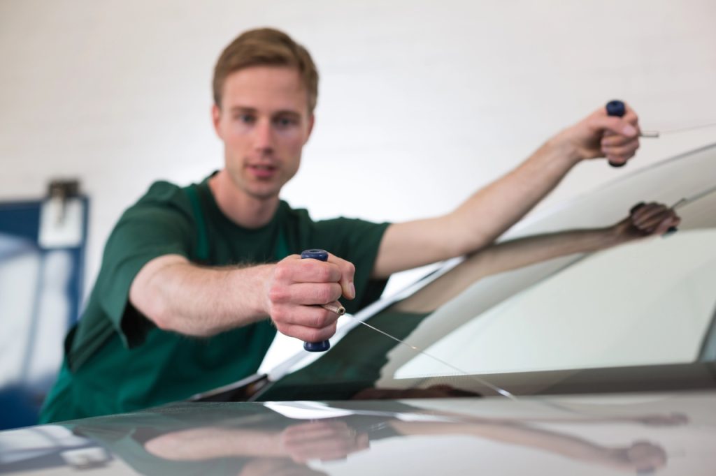 Expert auto glass repair Baltimore team performing a full windshield replacement on a vehicle using wire tools.