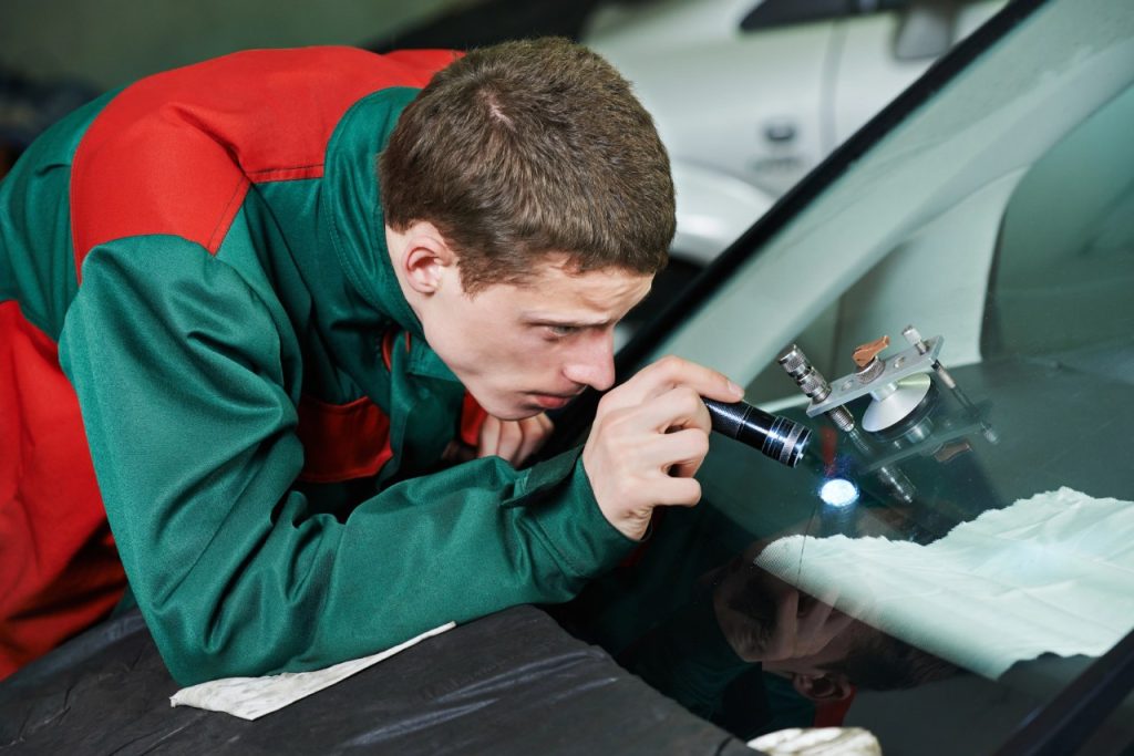 Professional auto glass repair Baltimore technician uses a flashlight to inspect a small windshield stone chip.