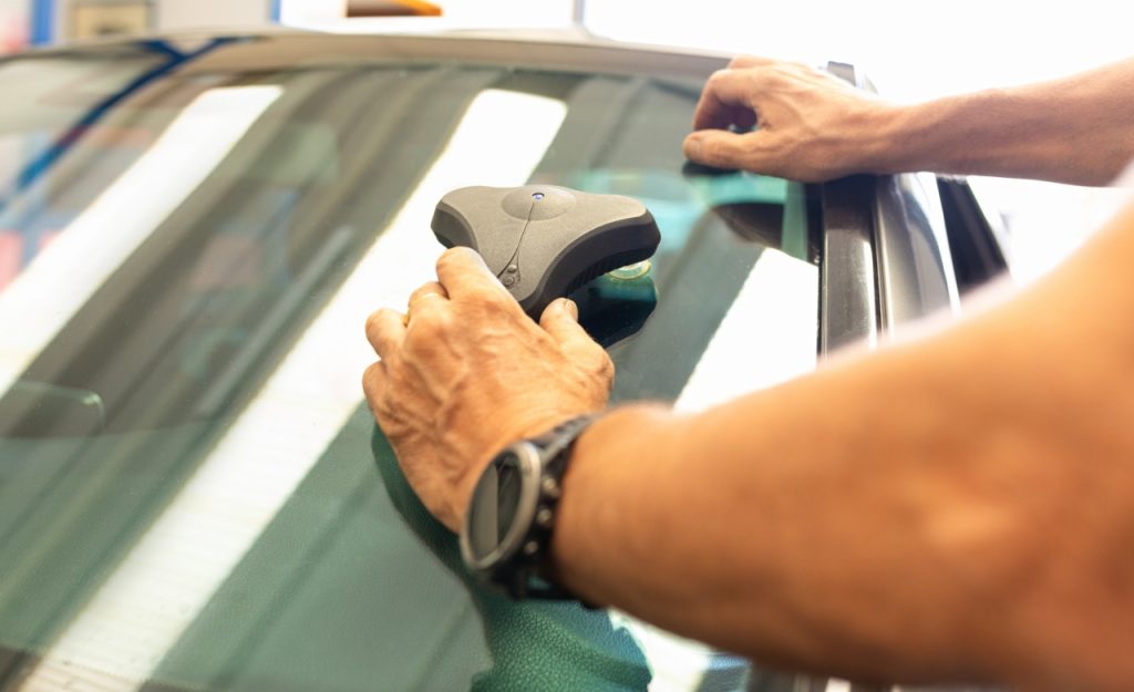 Specialist from an auto glass company Baltimore uses a resin injection tool to fix a cracked car windshield professionally.