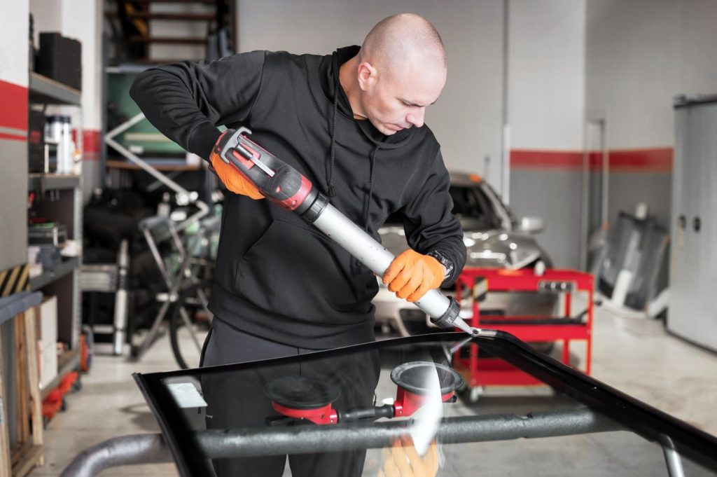 A technician at an auto glass shop Baltimore applying high-quality urethane adhesive to a new car windshield.