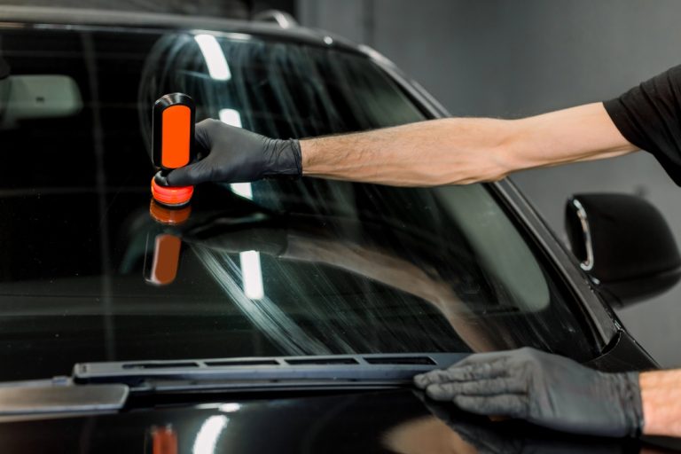 Specialist using a polishing tool for mobile auto glass repair Baltimore to remove scratches from a car’s windshield.