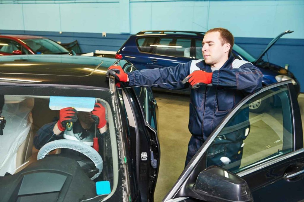 Technicians cutting the old seal during an auto glass replacement and repair Baltimore service in a shop.