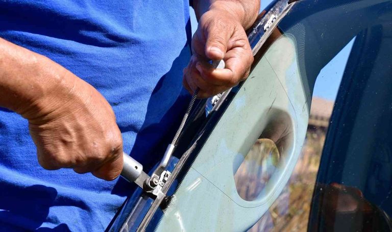 Professional at automotive glass shops Baltimore uses specialized cutting wire tools to remove a broken windshield.
