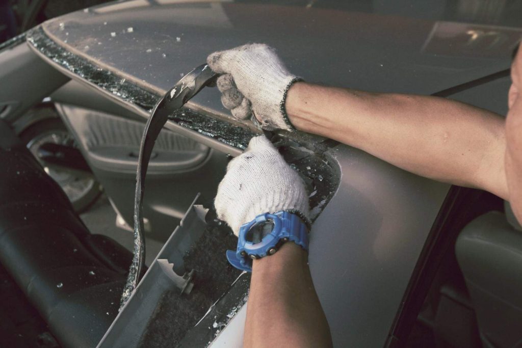 Technician at automotive glass shops Baltimore removes old sealant and broken glass from a car window frame. 