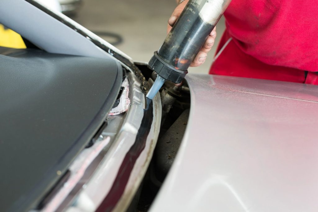 Auto glass technician at a windshield repair shop Baltimore applying black urethane adhesive sealant to a car frame. 