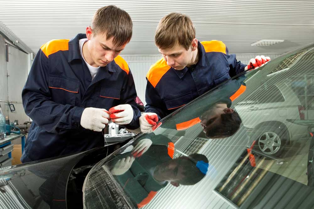 Auto glass technicians carefully sealing a car windshield during a mobile auto glass repair Baltimore project.